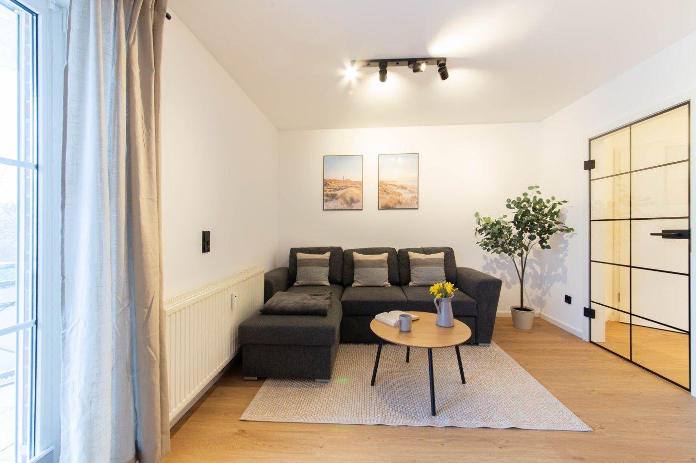 Ein Wohnzimmer mit grauem Sofa, Holztisch und Pflanze.