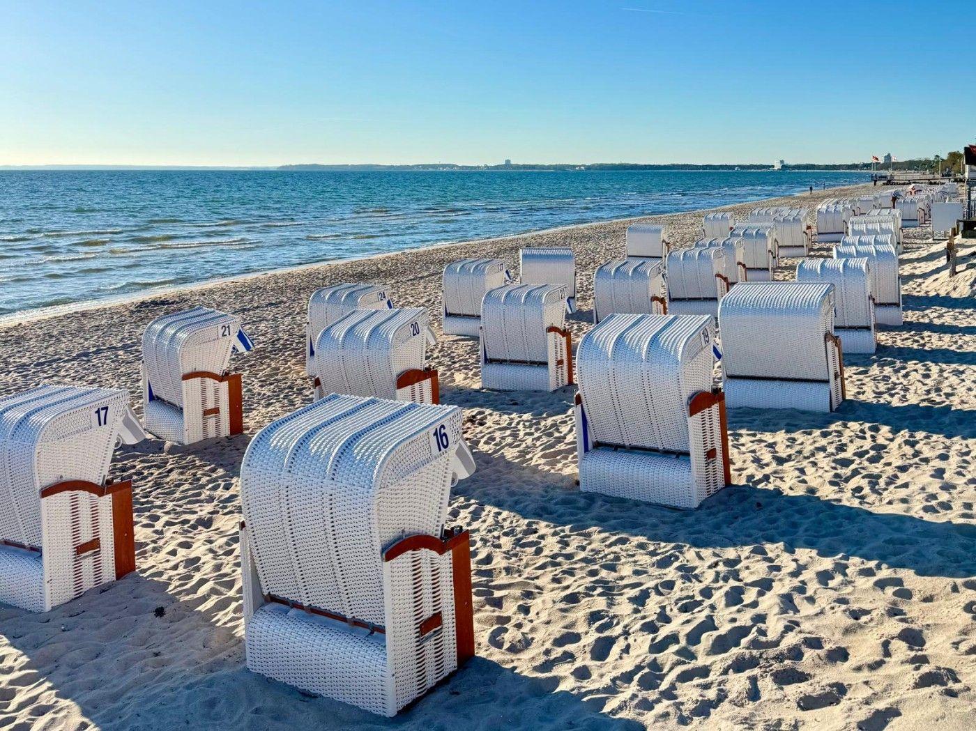 Weiß lackierte Strandkörbe auf Sandstrand mit Blick auf Meer und Horizont.