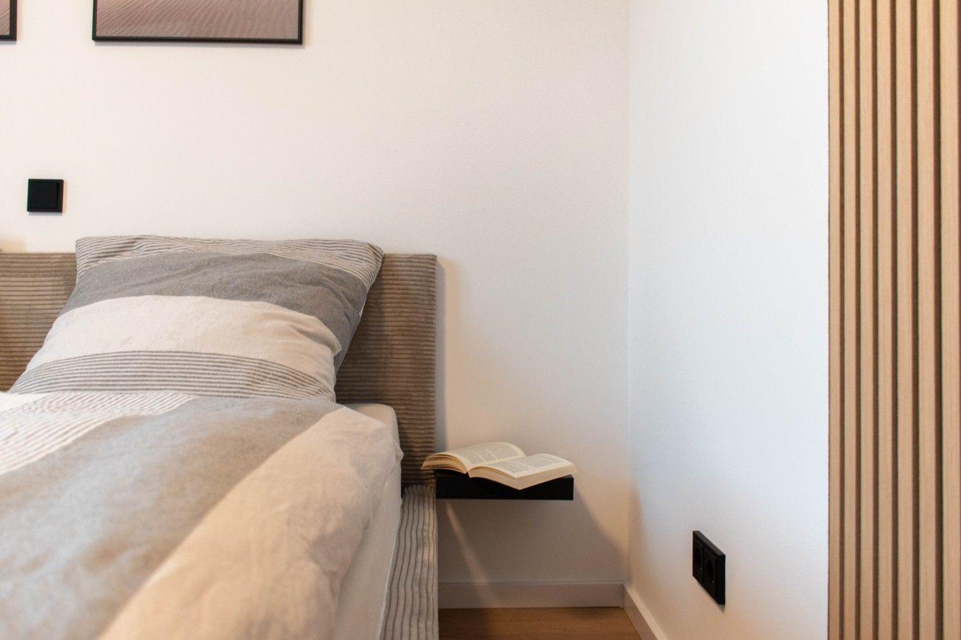 Schlafzimmer mit Bett, Kissen und offenem Buch auf Nachttisch.