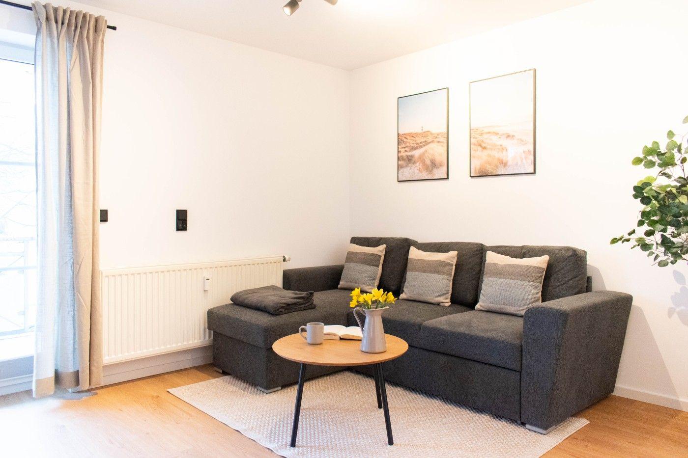 Ein Wohnzimmer mit grauem Sofa, Holztisch und Wandbildern.