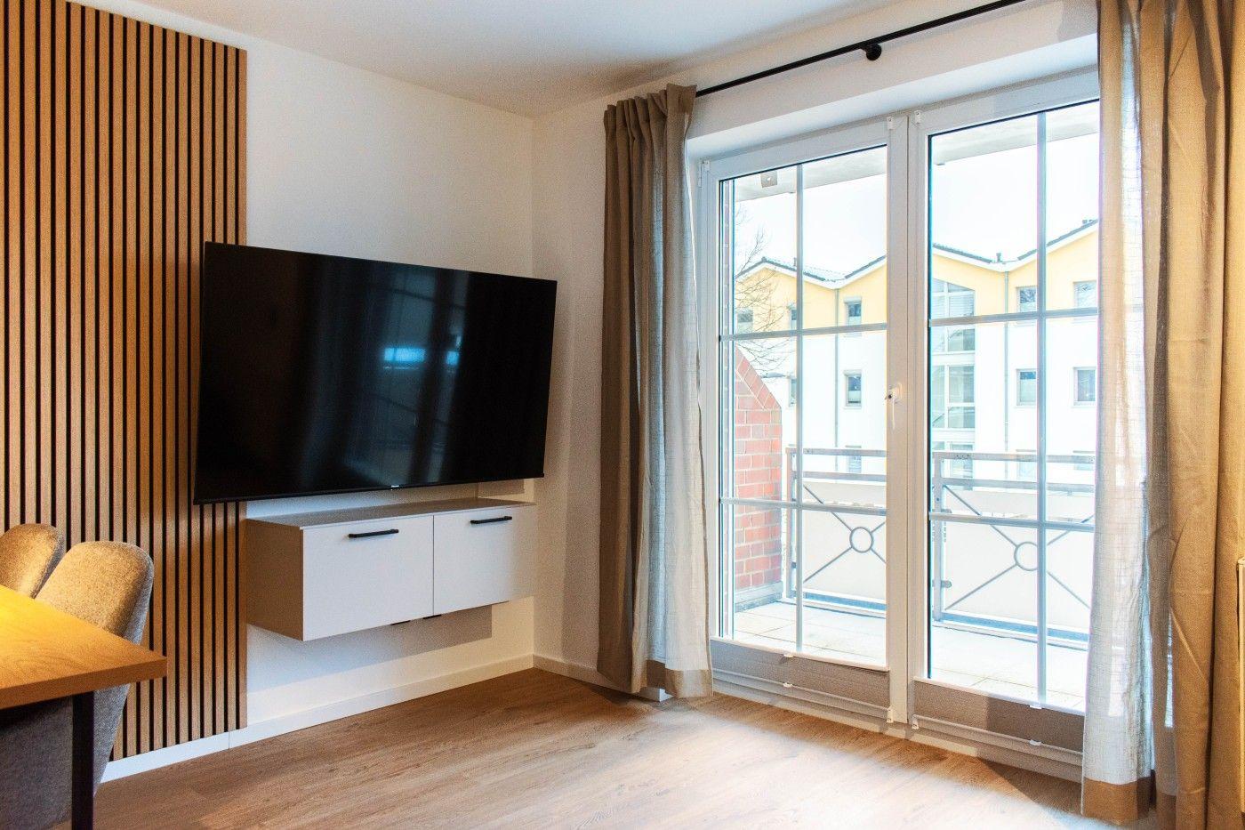 Wohnzimmer mit TV, Balkon und Holzboden