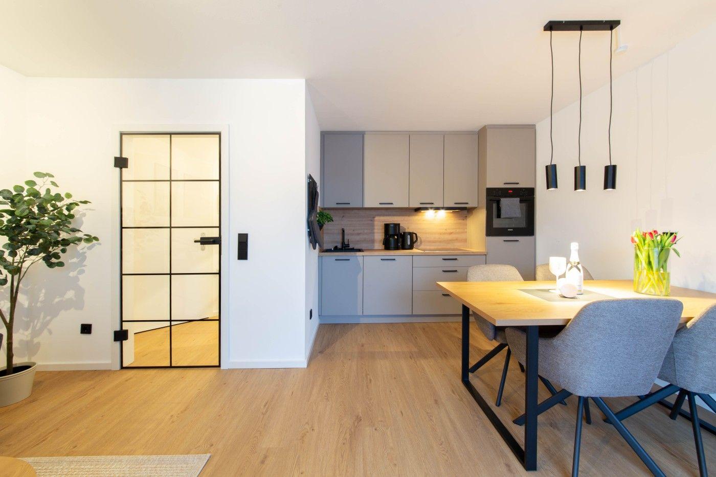 Moderne Küche mit Essbereich und Glaswand. Holzboden und schlichte Möbel.