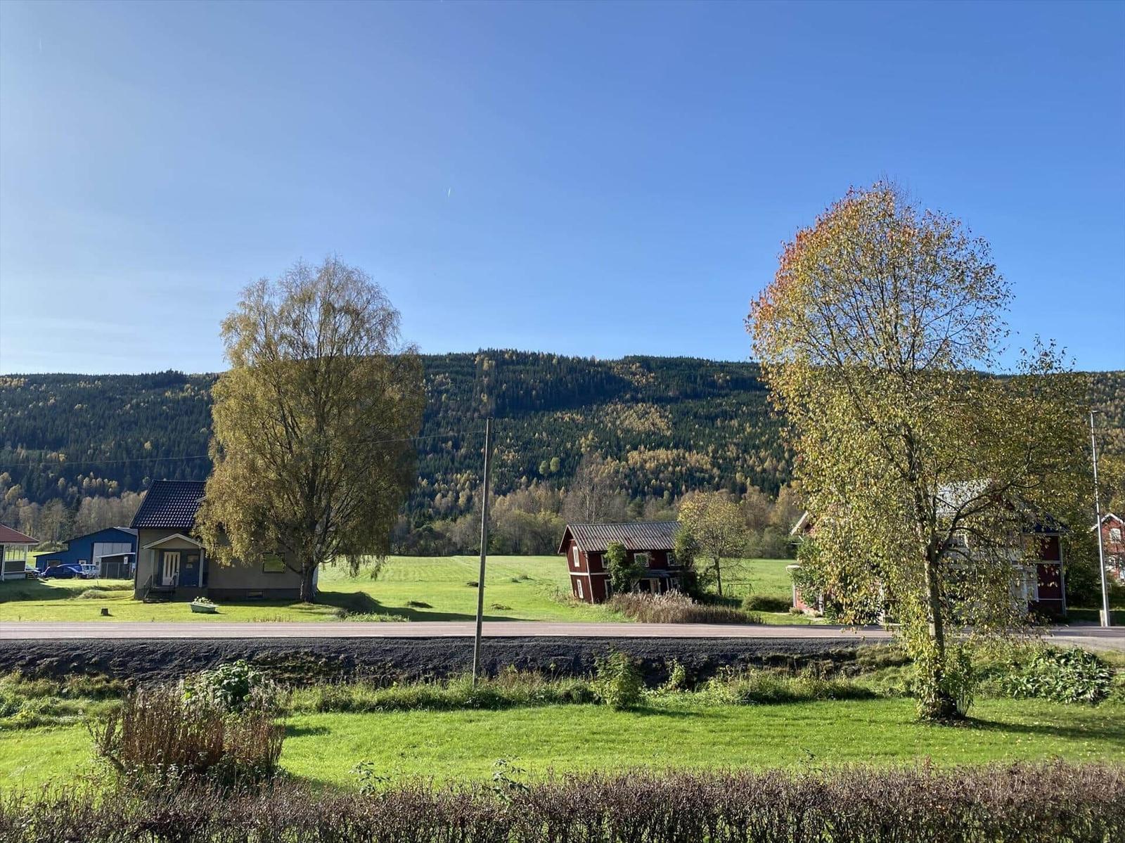 Haus mit Blick auf grüne Wiesen und bewaldete Berge unter blauem Himmel.