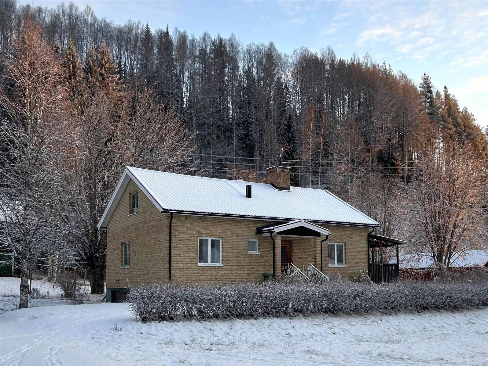 Ein Haus mit Schneebedecktem Dach und Holzveranda vor einem Wald.