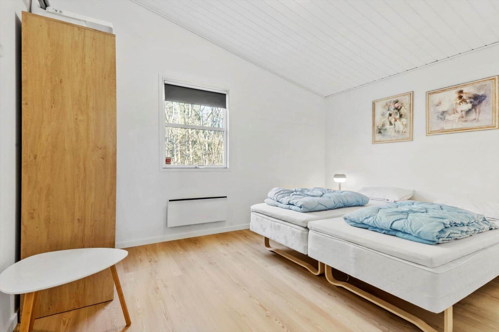 Two beds with blue blankets, window, wooden floor, and wall pictures.