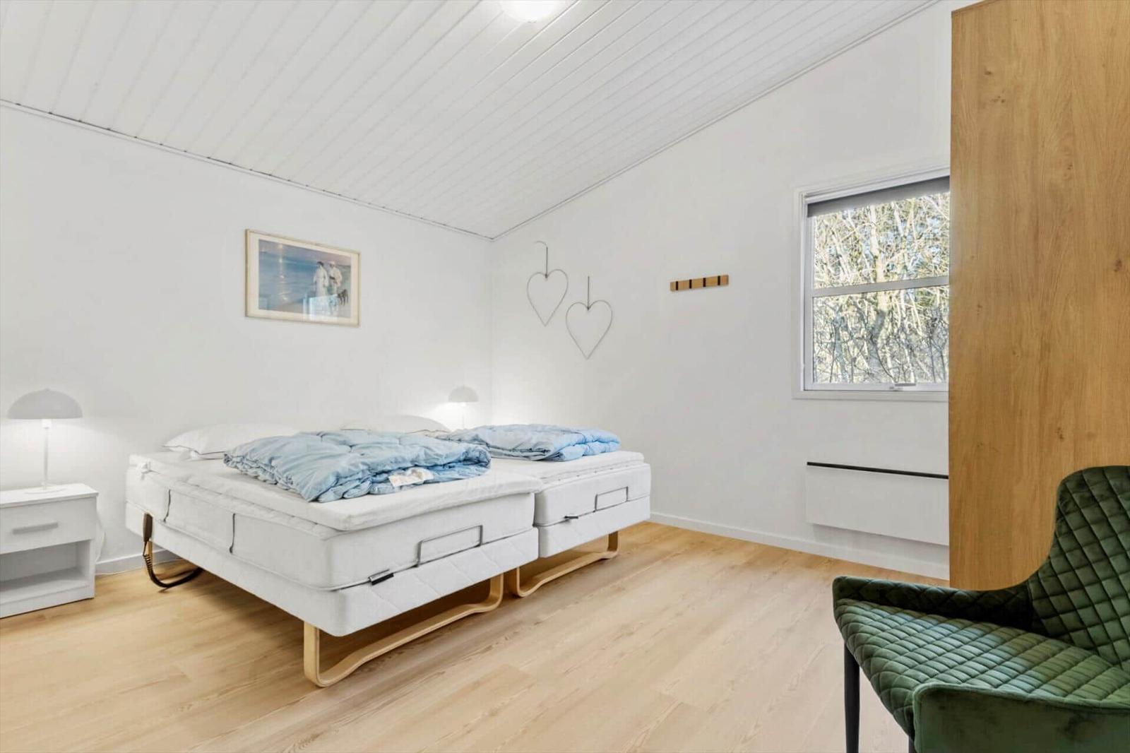 Room with double bed, green armchair, and window with tree view.