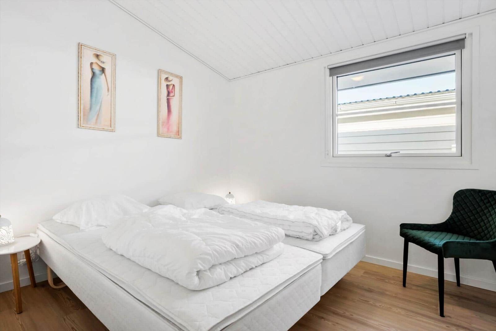 Room with double bed, green chair, and window.