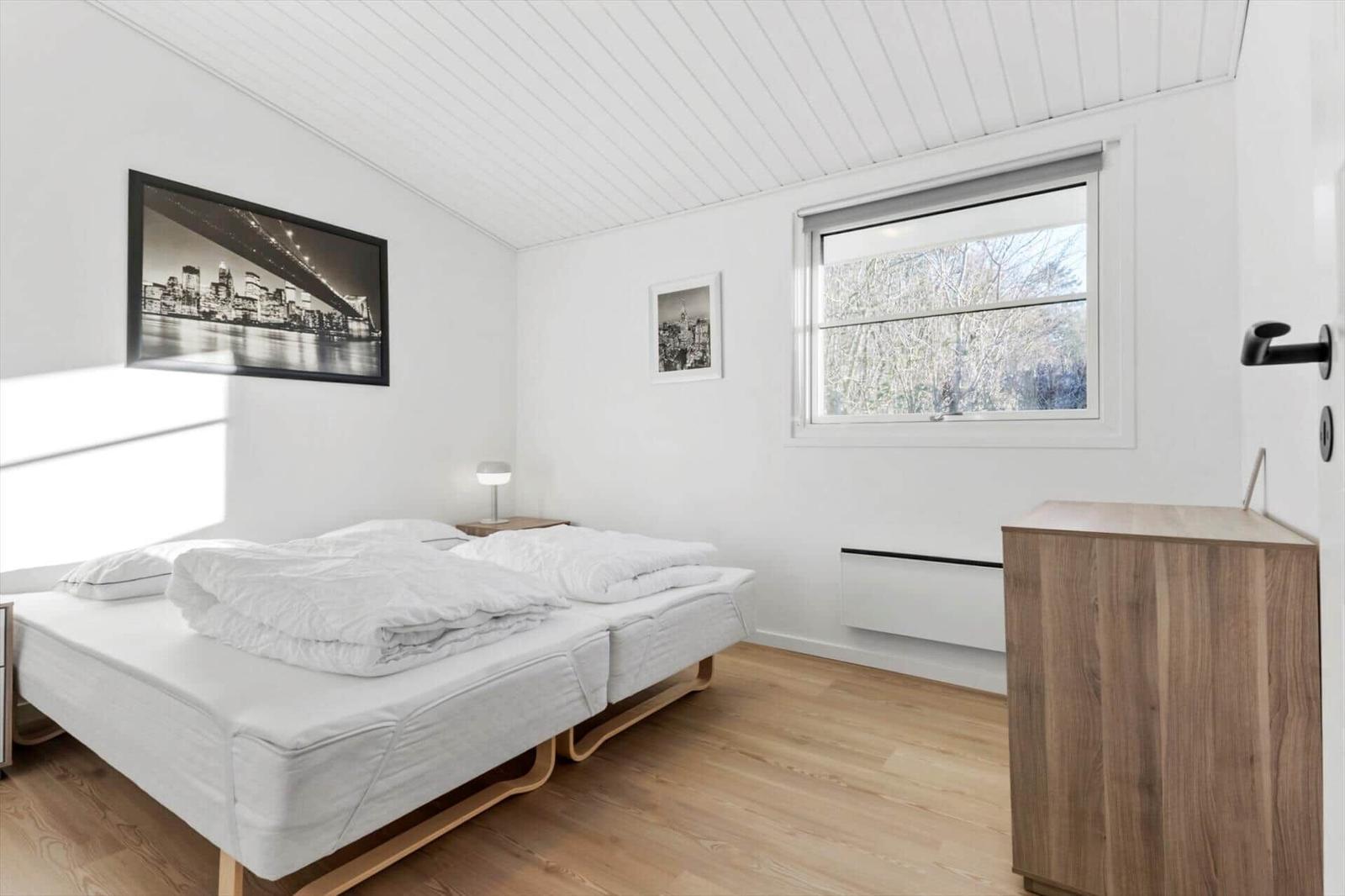 Bedroom with double bed, wooden floor, and window with view of trees.