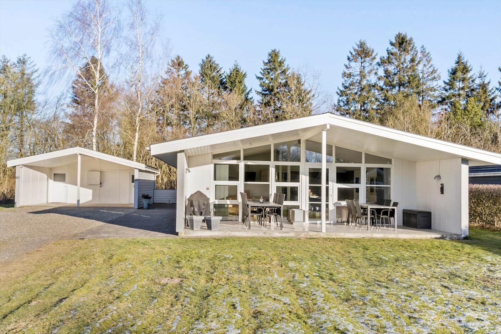 Modern white villa with large terrace and garden. Forest in the background.