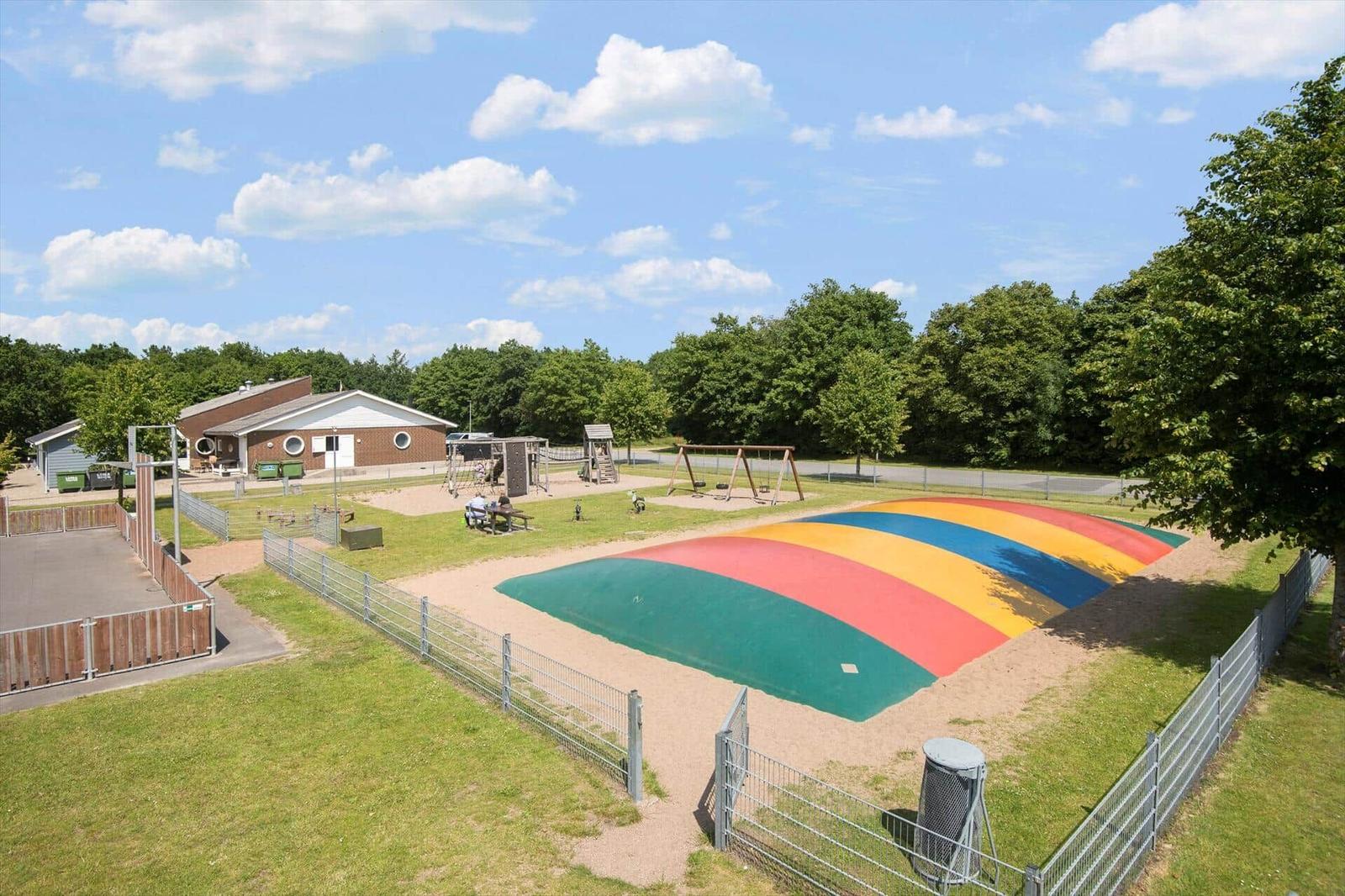 Large playground with colorful sand area and swing set. Background: buildings and trees.