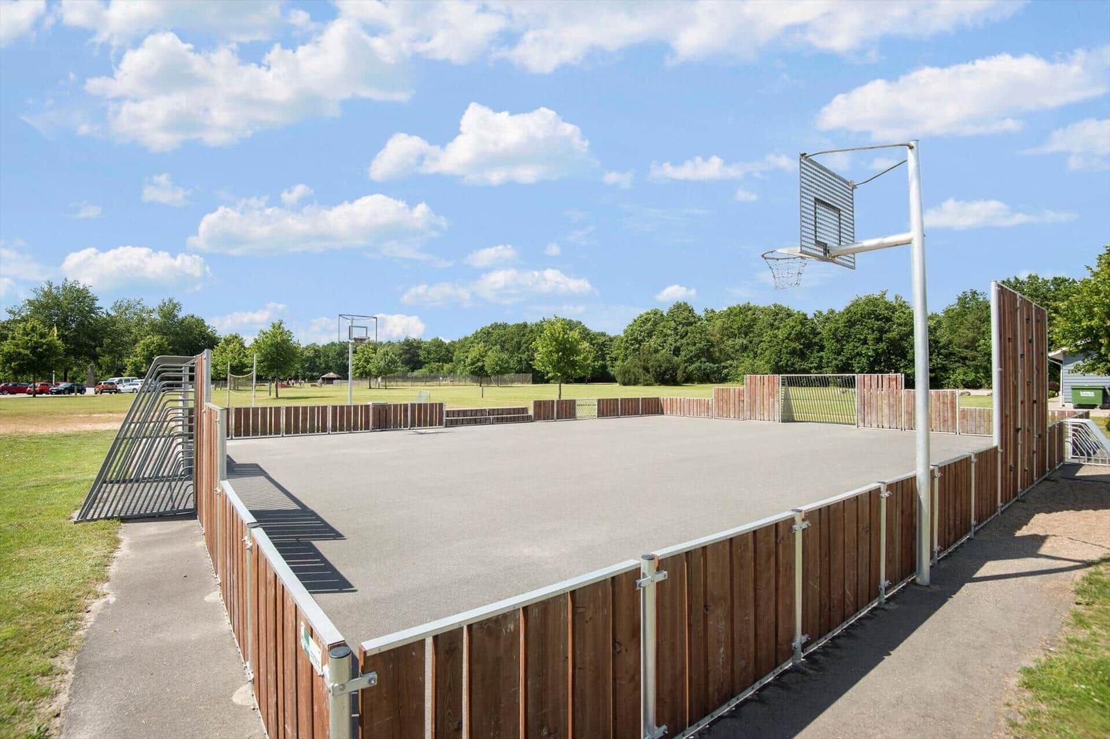 Basketball court with wooden fencing and hoop under blue sky.