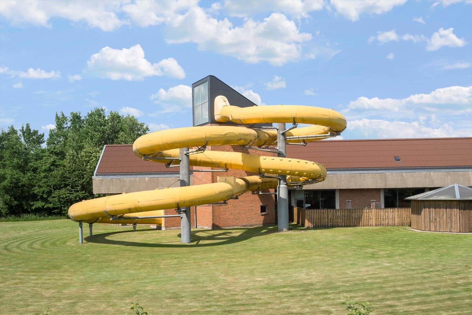 Yellow water slide in front of a building with a red roof.