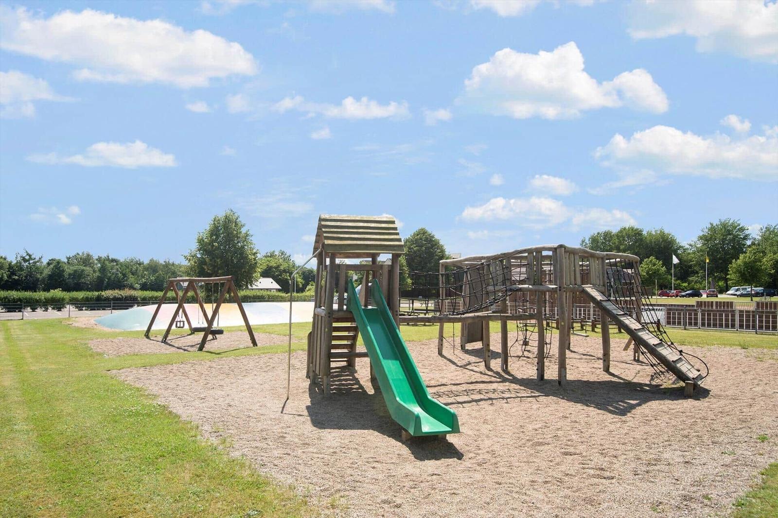 Large playground with slide, climbing frame, and swing on sandy ground under blue sky.