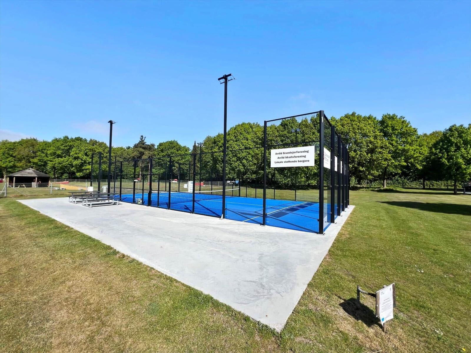 Blue paddle tennis court with fencing and benches outdoors.