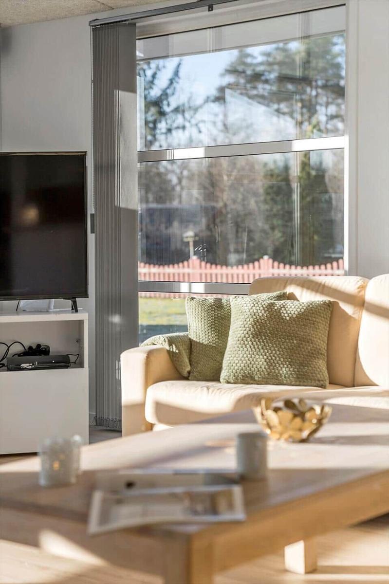 Living room with sofa, coffee table, and TV. Large windows with view of garden.