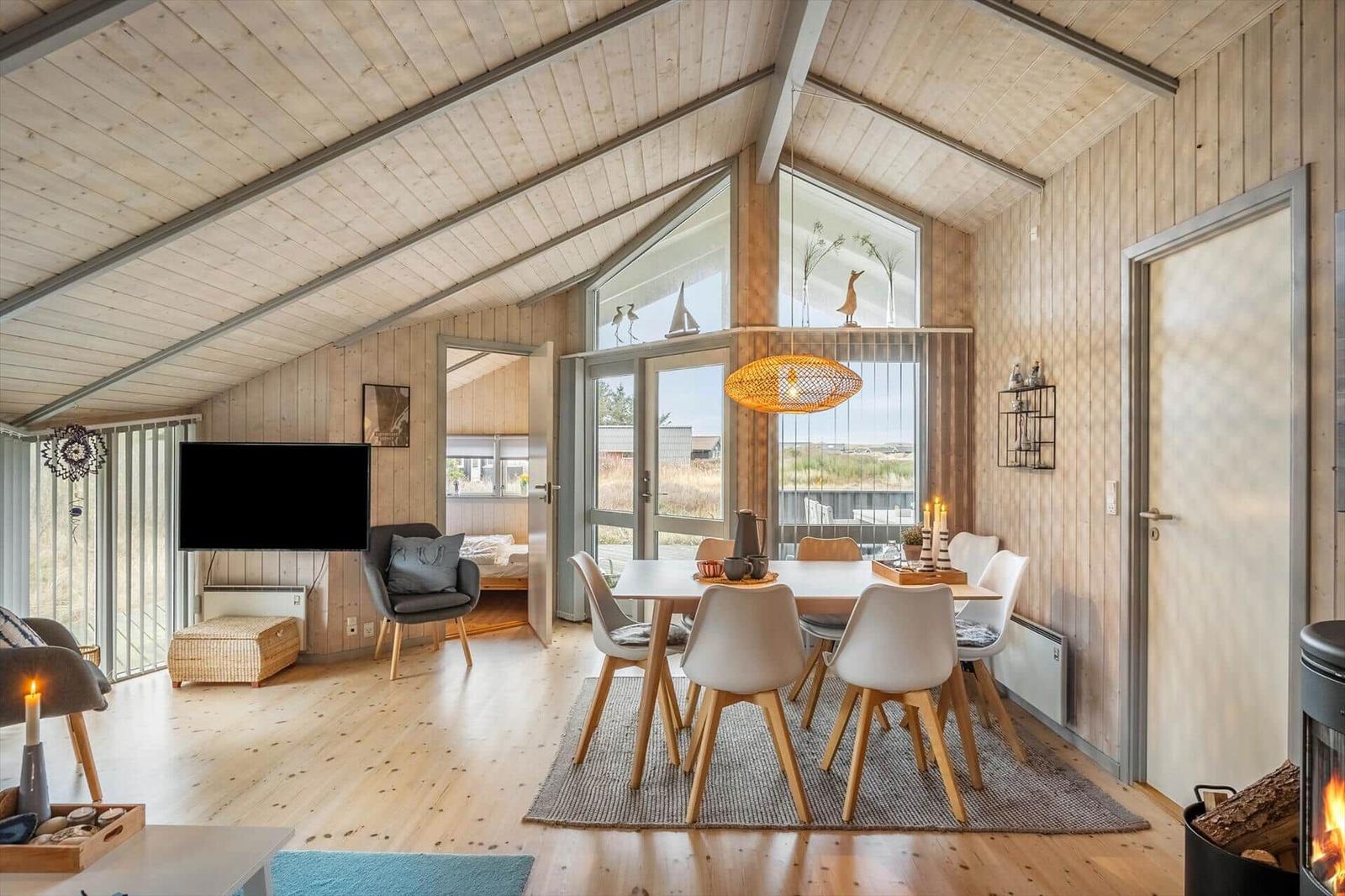 Living and dining area with wood paneling, dining table, TV, and wood stove.