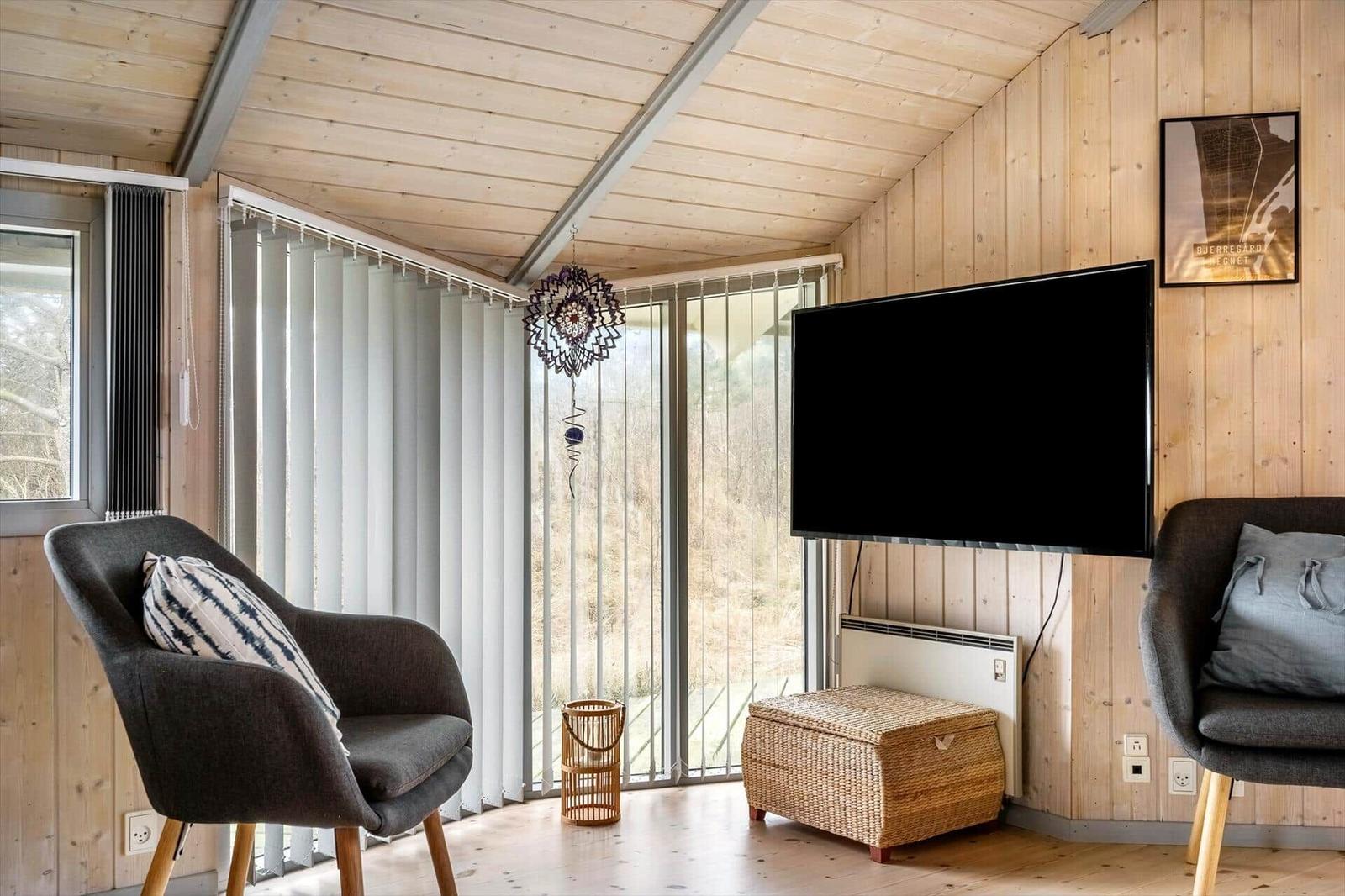 Living room with wooden walls, TV, two armchairs, and view of nature.