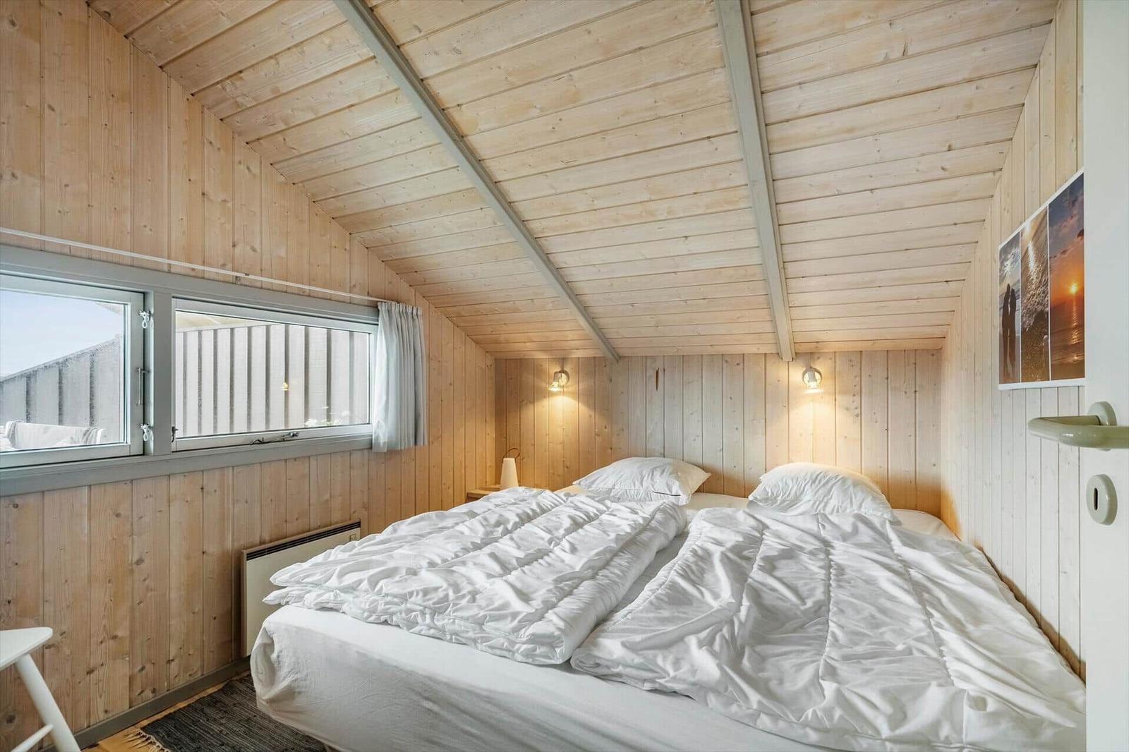Bedroom with wooden walls and double bed. Window and wall lights visible.