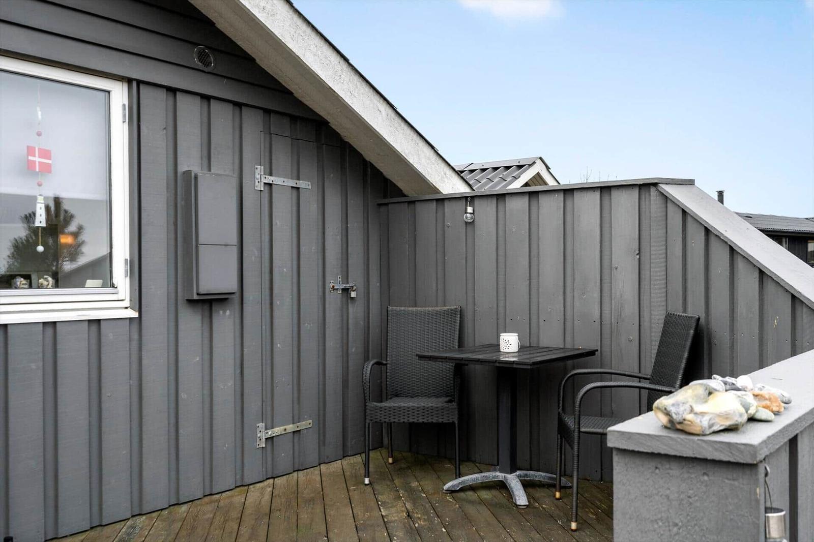 Terrace with table and two chairs, wooden floor and gray wood wall.