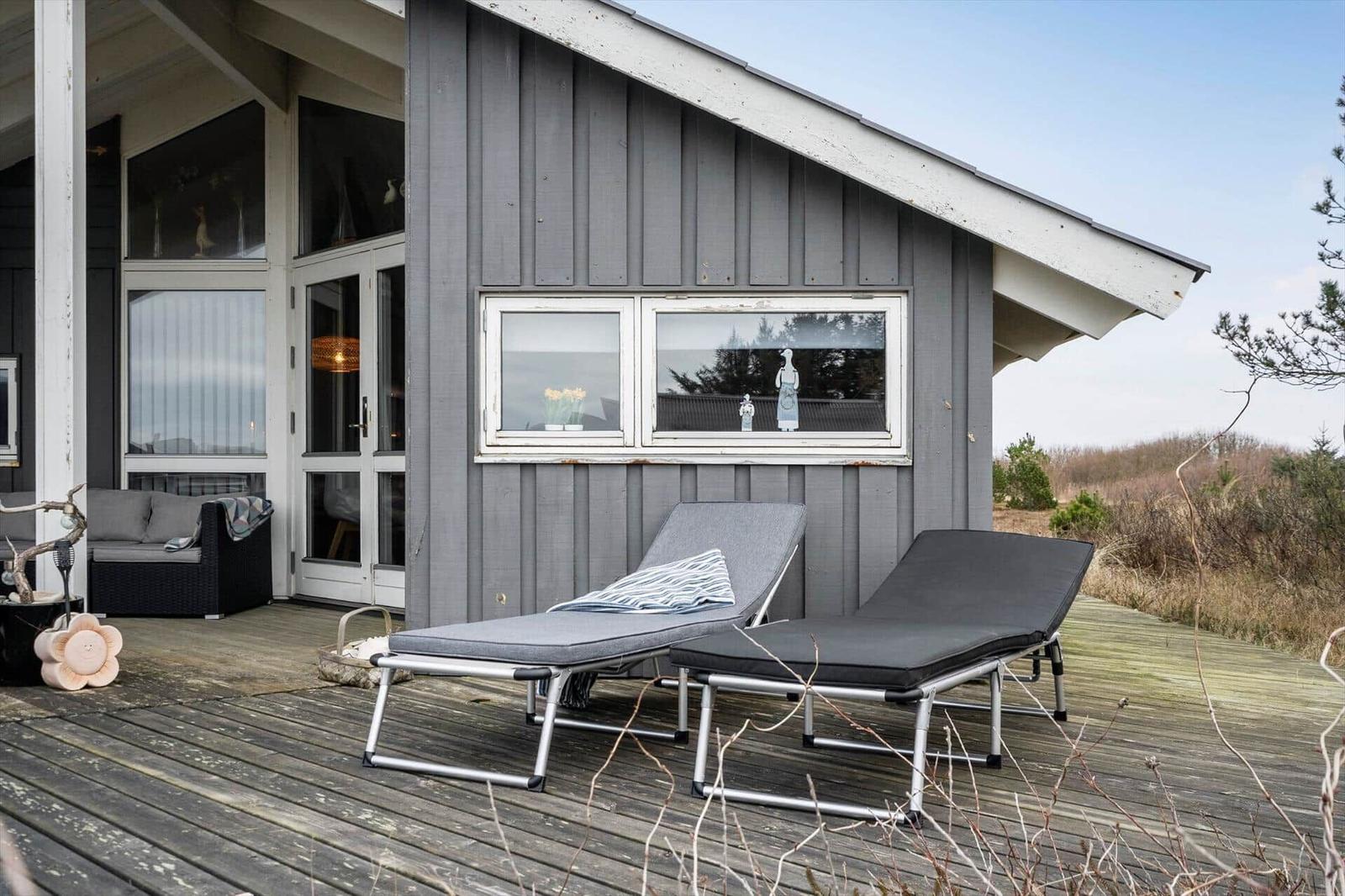 Deck with two lounge chairs in front of gray wooden house with windows.