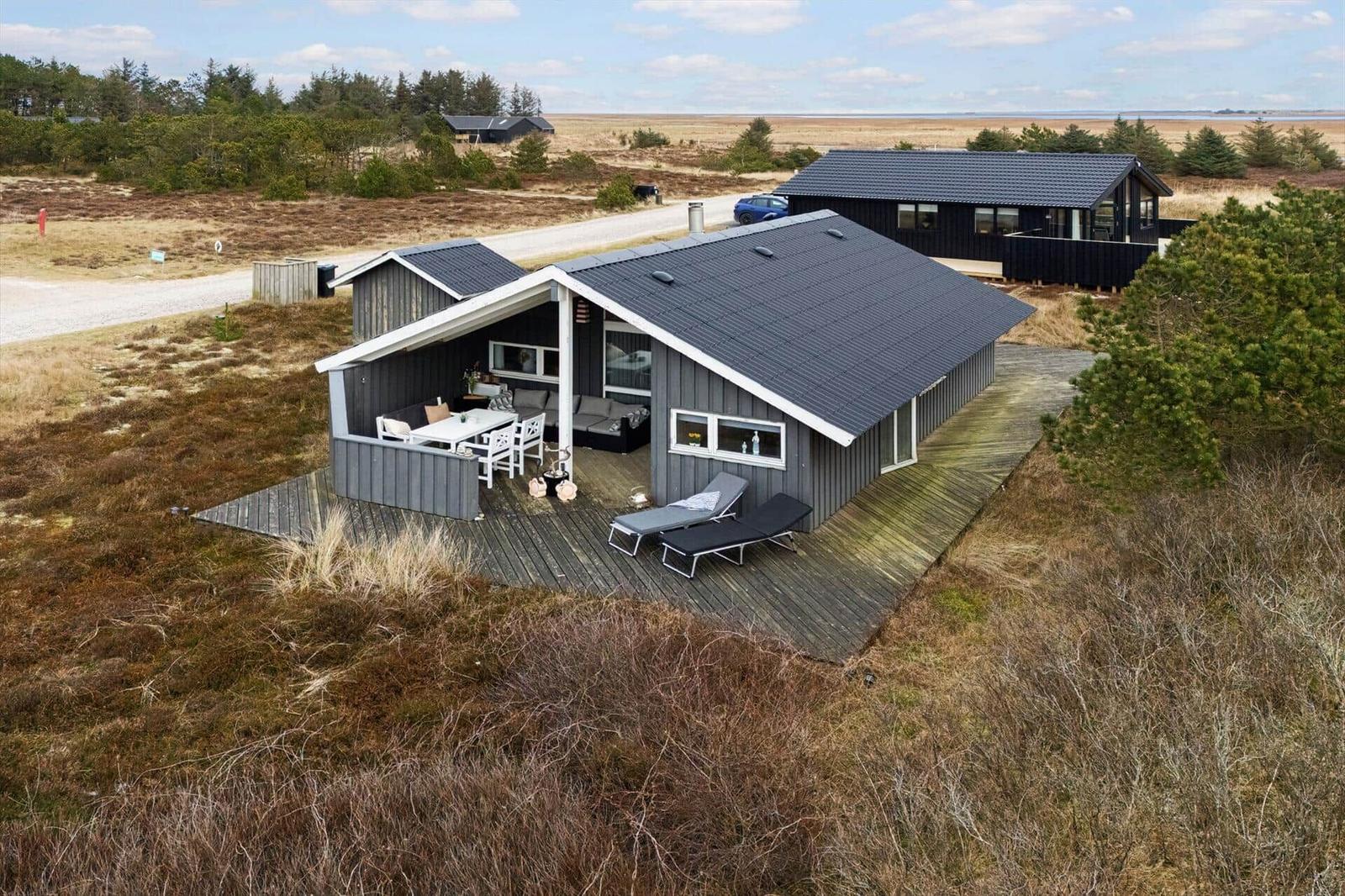 Modern wooden cabin with terrace and sun loungers. View of open land.