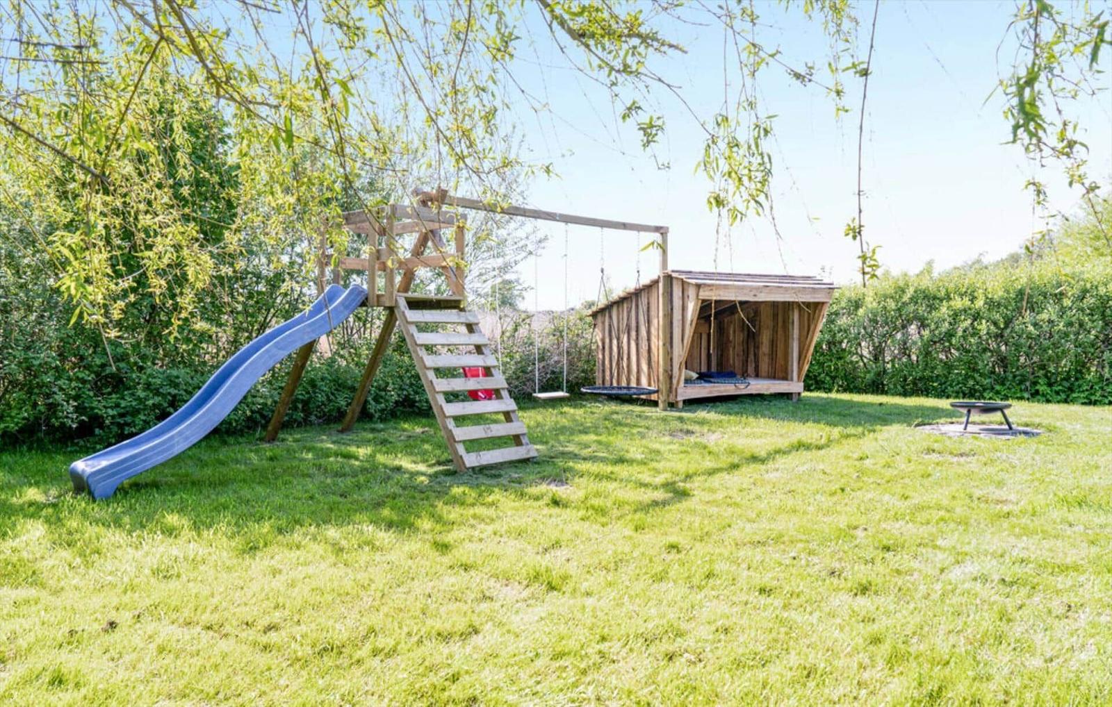 Backyard with climbing frame, slide, swing, and wooden hut.