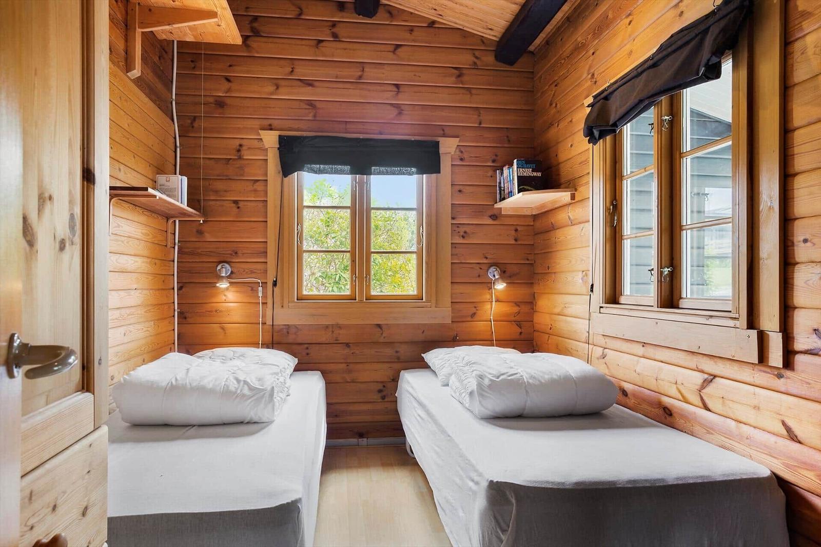 Two beds in a wooden house room with windows and wall shelves.