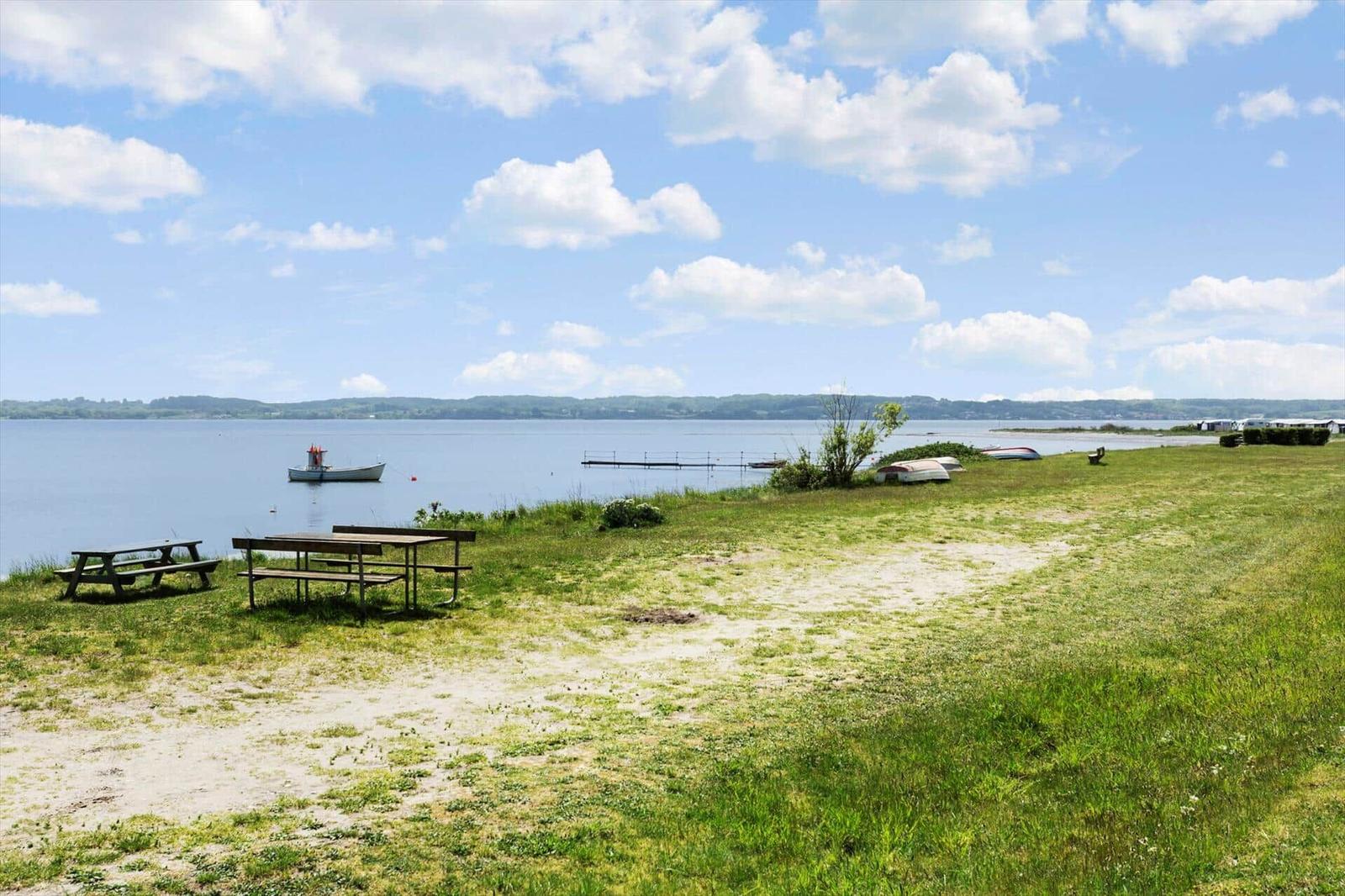 Green lakeside area with picnic tables and boats on the water.