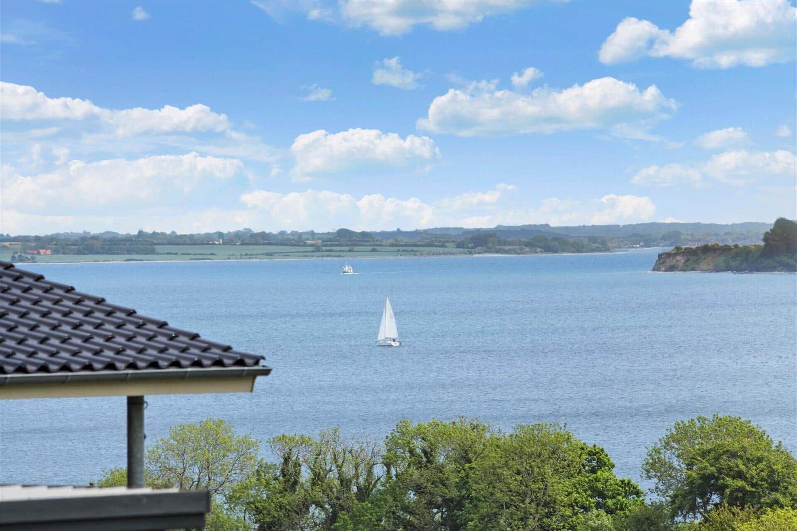 Wide view of the sea with sailboats and green landscape in the background.
