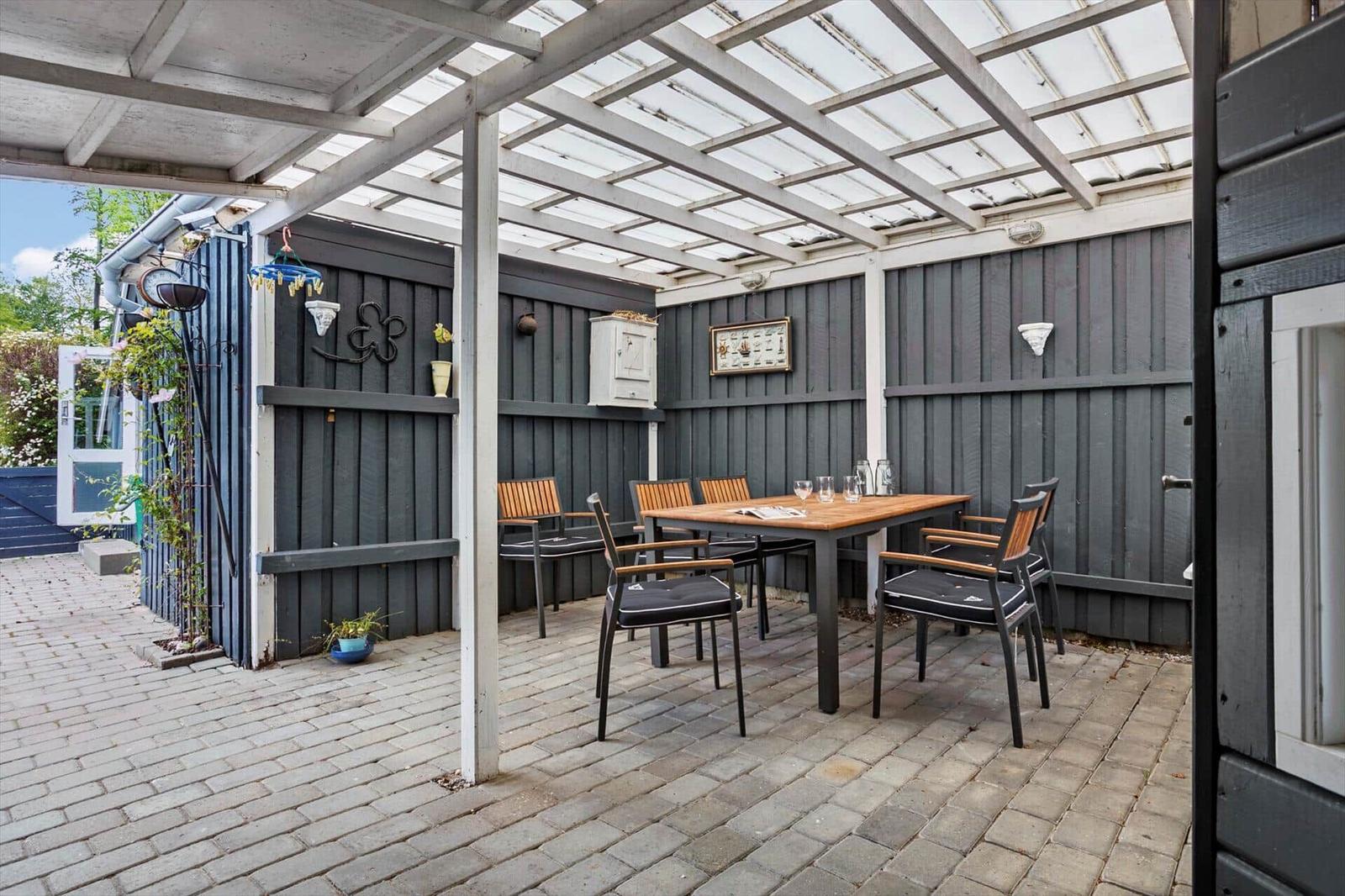 Terrace with seating under glass roof, paved and with walls of dark wood.