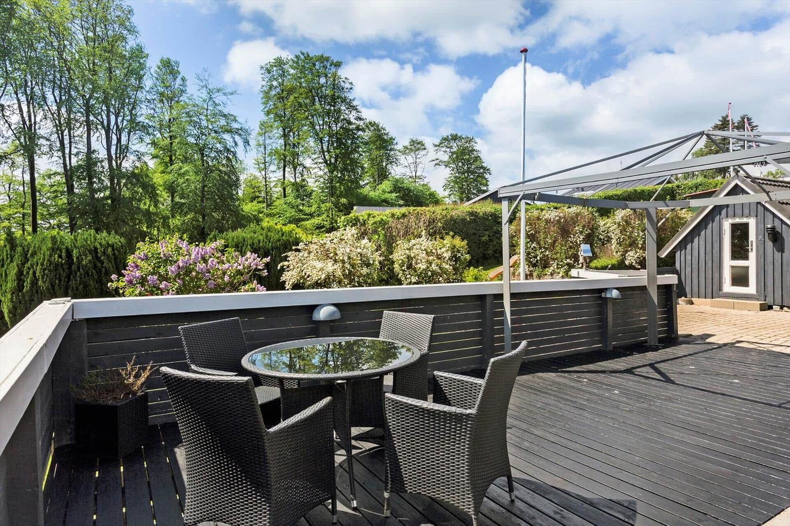 Deck with table and chairs, view of green trees and shrubs.