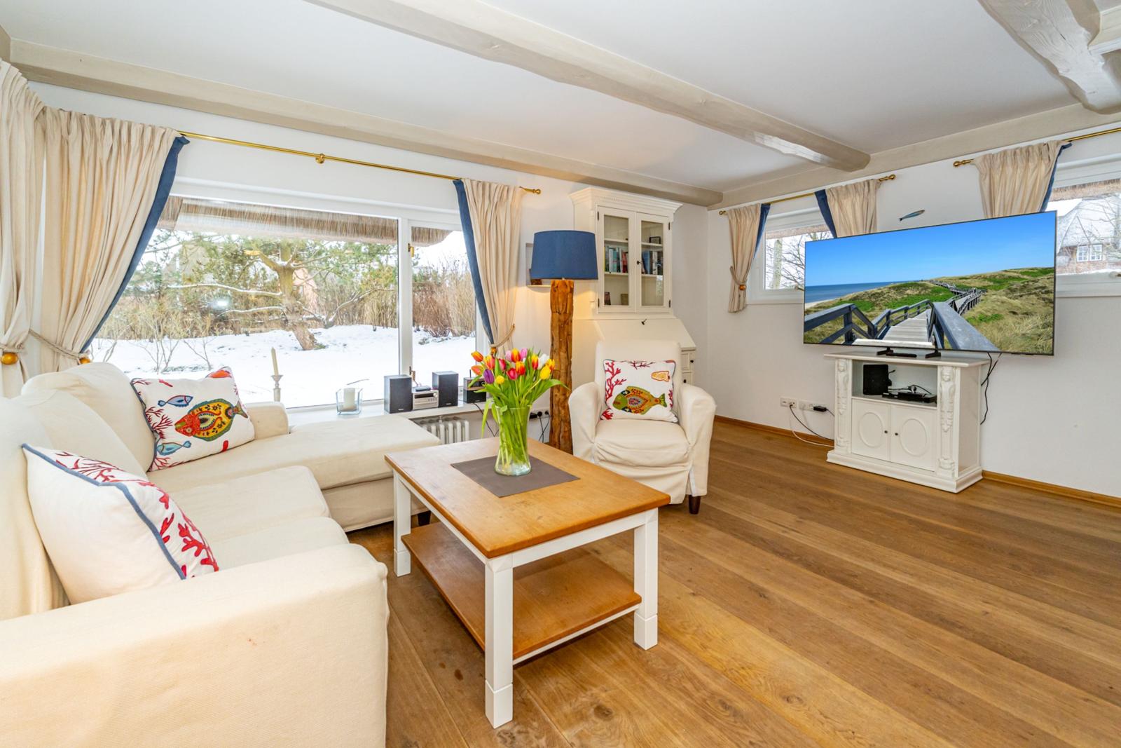 Wohnzimmer mit Sofa, Sessel, Couchtisch und Fernseher an der Wand.