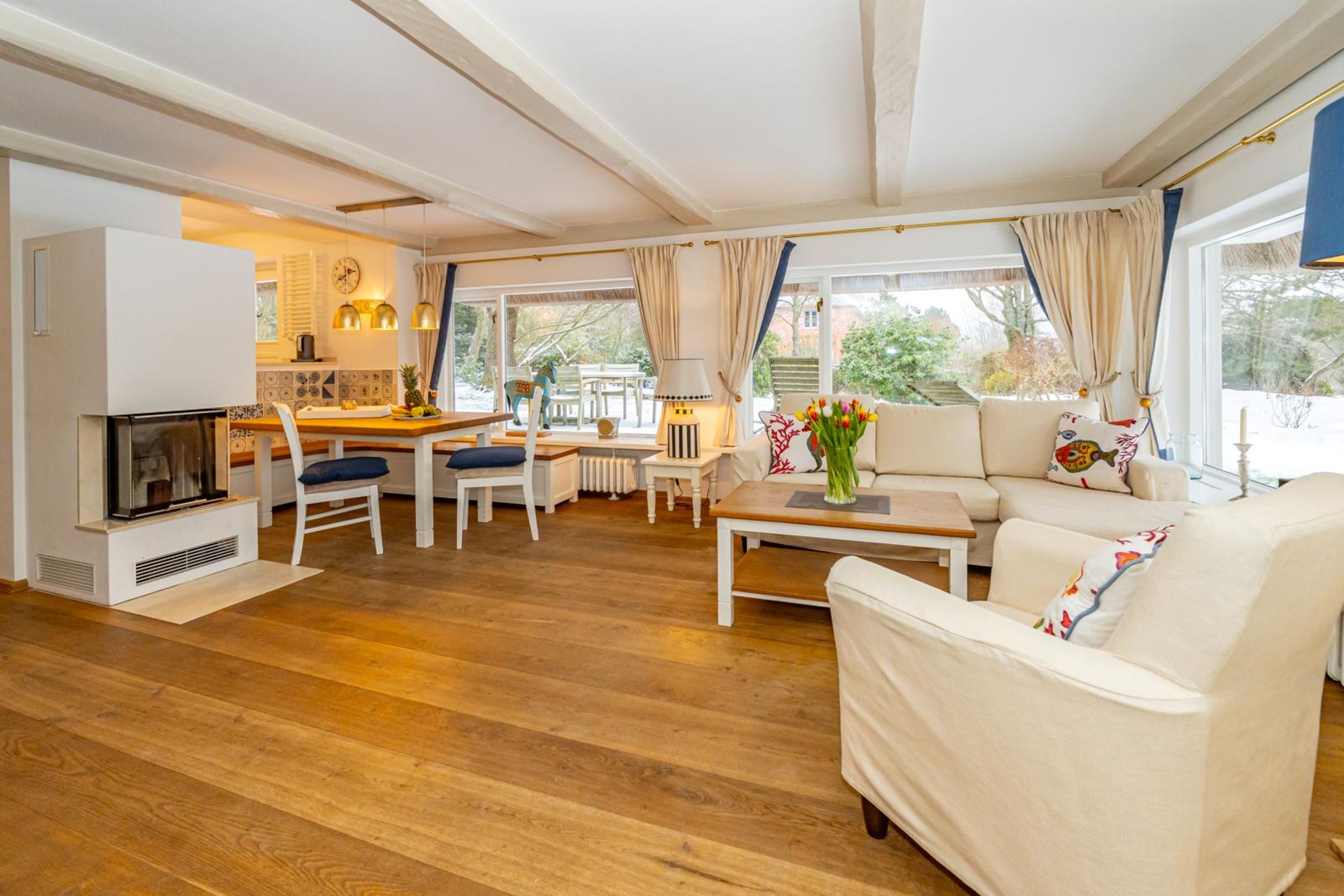 Wohn- und Essbereich mit Holzboden, Sofa, Kamin und großem Fenster.