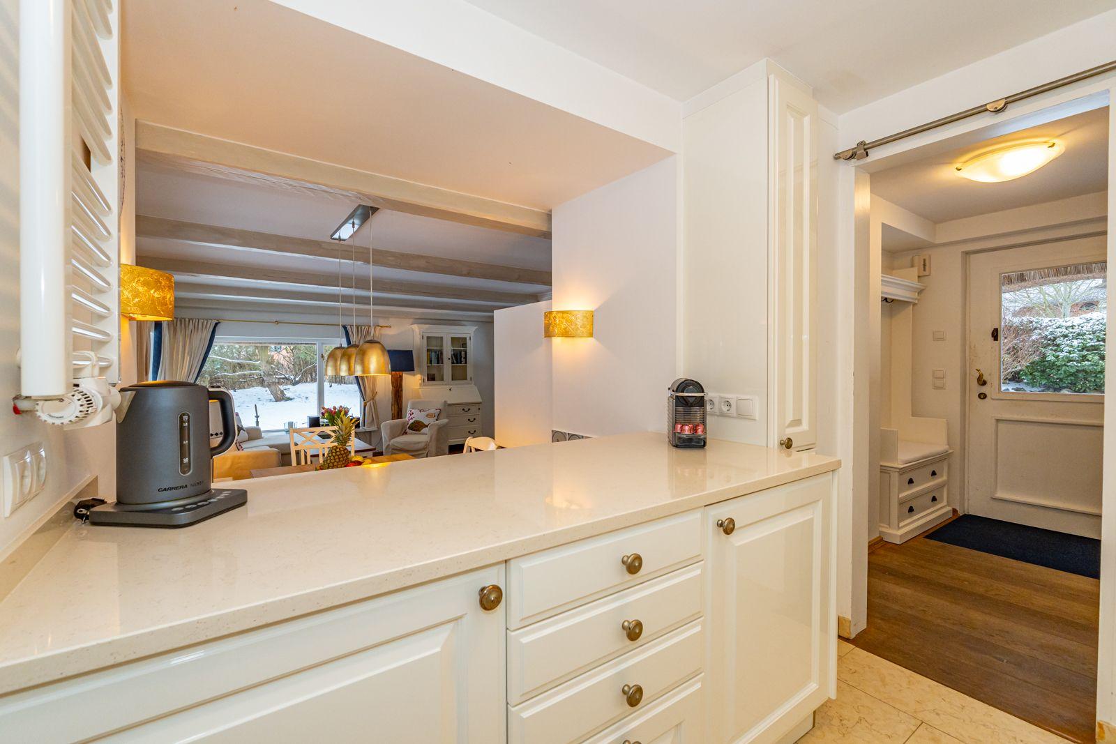 Küche mit Arbeitsfläche, Kaffeemaschine und Blick ins Wohnzimmer.