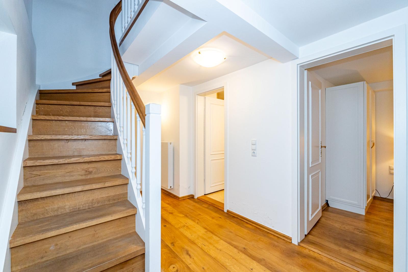 Haus mit Holztreppe und Holzboden. Treppe führt nach oben. Türen zu Räumen sind sichtbar.