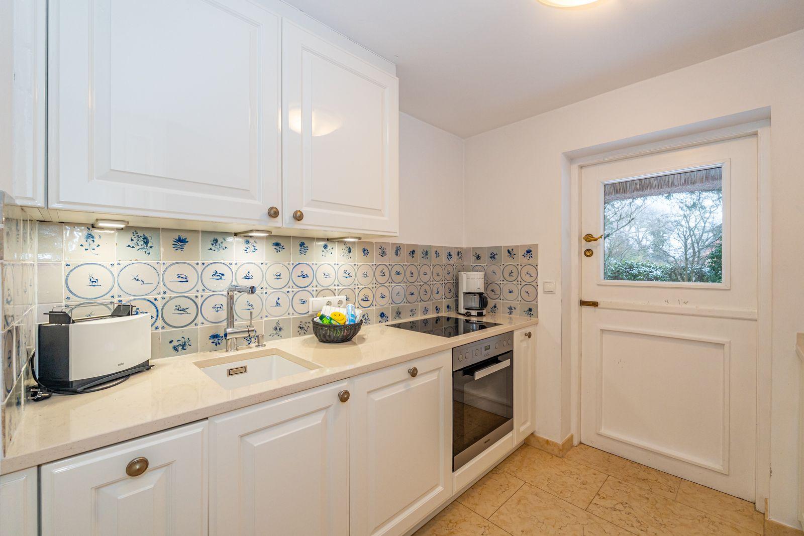 Küche mit weißen Schränken, blau-weißem Fliesenspiegel und integriertem Herd.