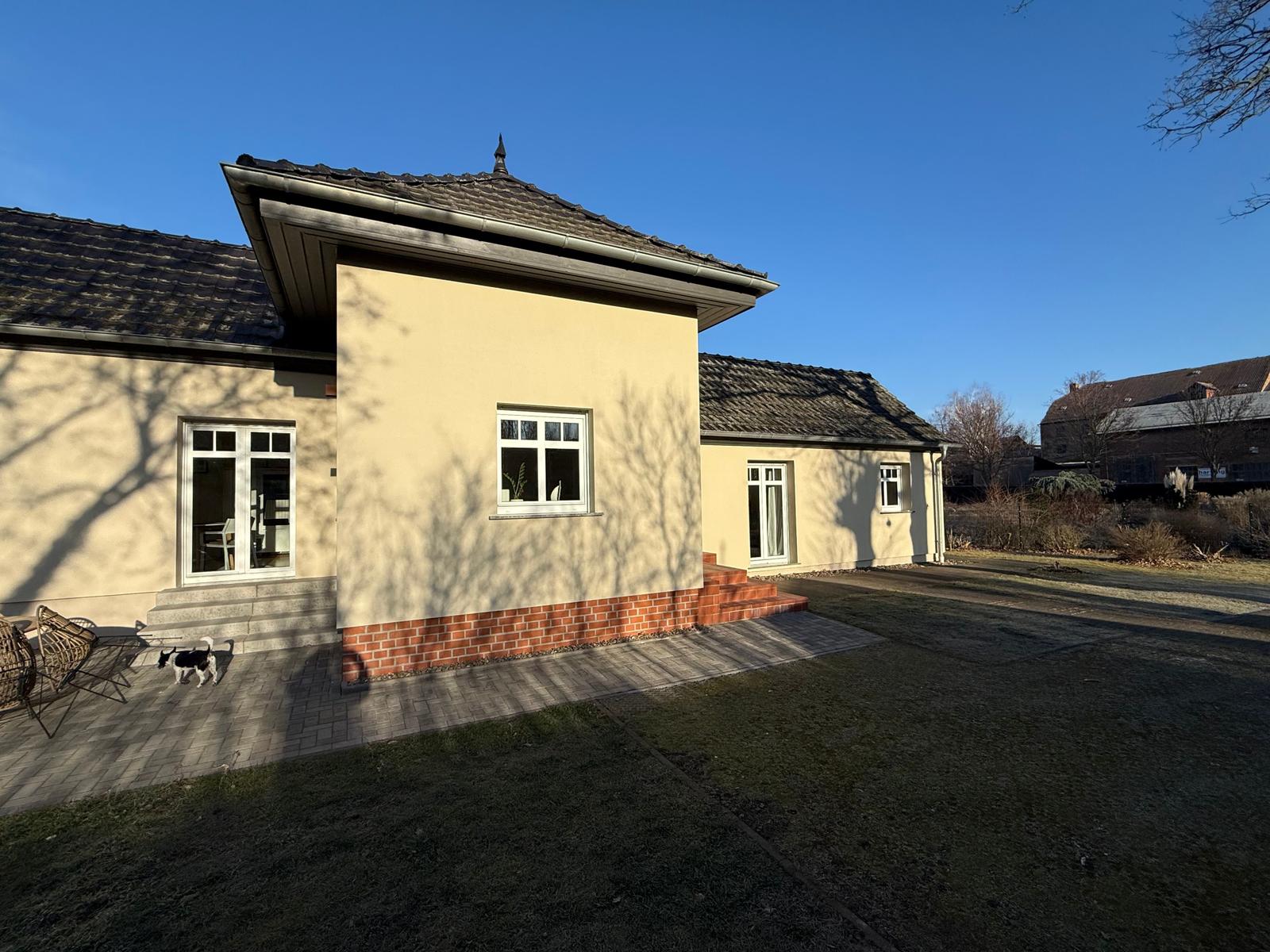 Haus mit Terrasse, Garten und Fenstern. Eine Katze läuft auf dem Hof.