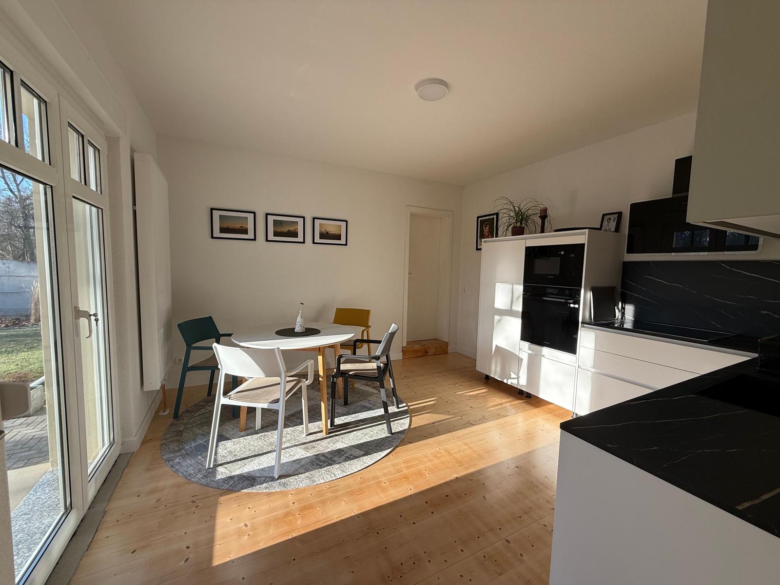 Küche mit Essbereich, Holzboden und Glastür zum Außenbereich.