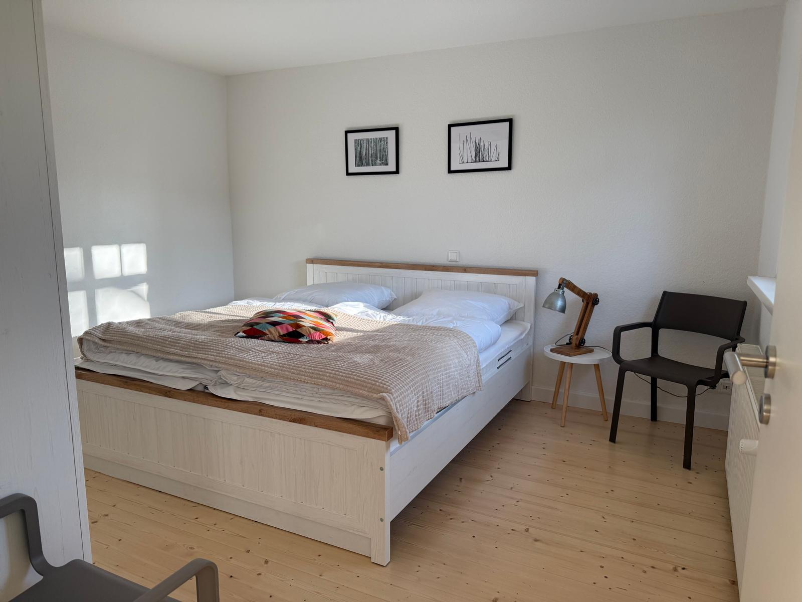 Schlafzimmer mit Bett, Stuhl und Lampe an der Wand.