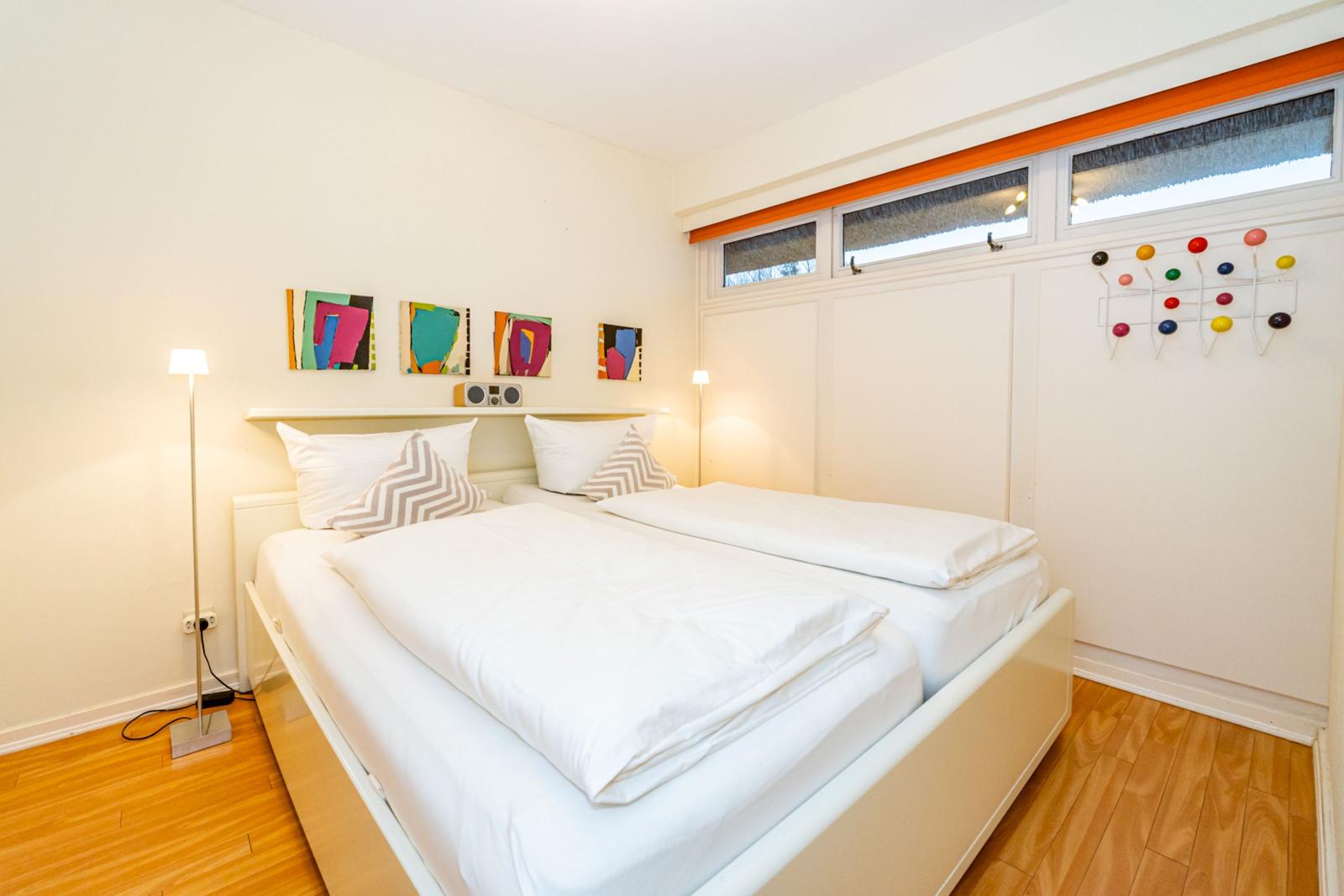 Zimmer mit Doppelbett, Holzboden und Fenstern mit Jalousien.