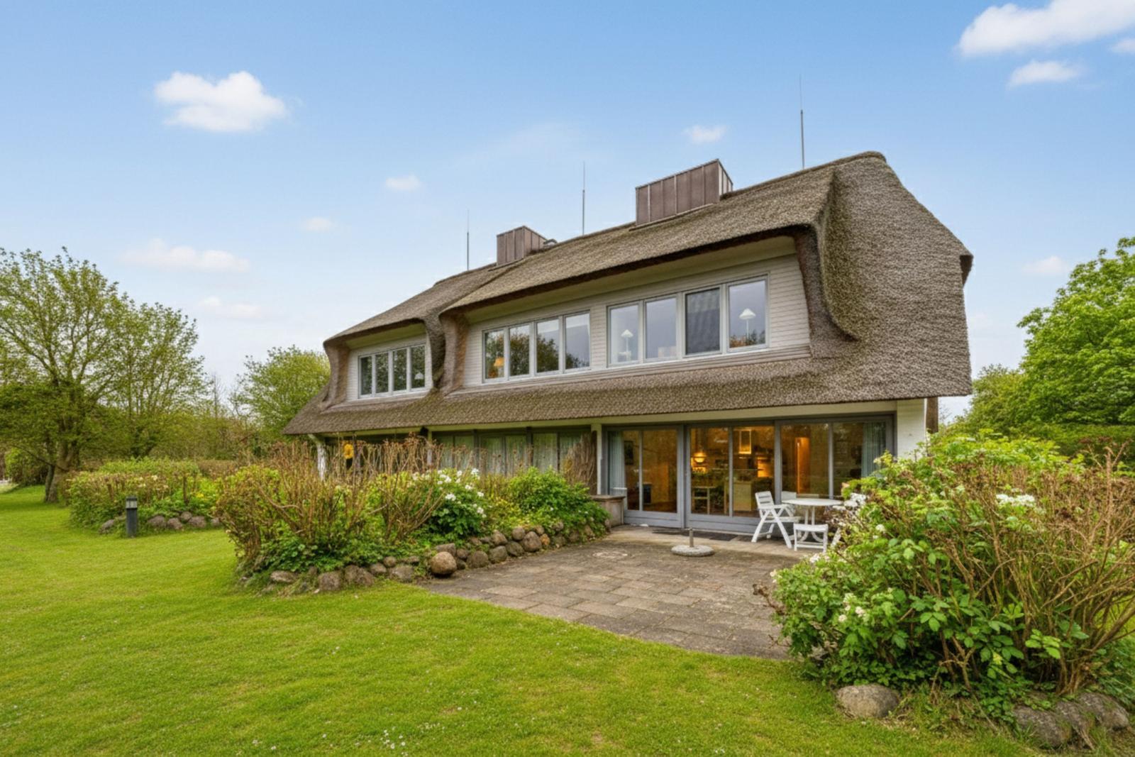 Haus mit Strohdach, großem Garten und Terrasse mit Tisch und Stühlen.