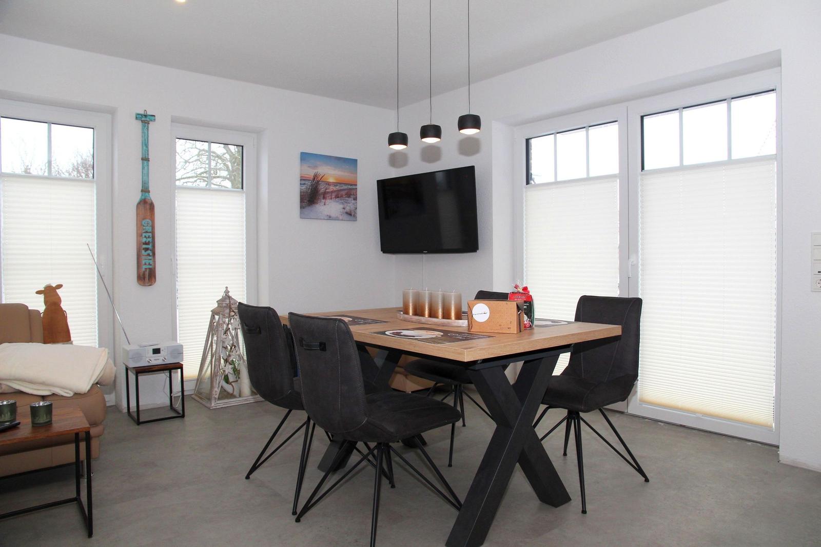 Esszimmer mit Holztisch, schwarzen Stühlen und TV an der Wand.