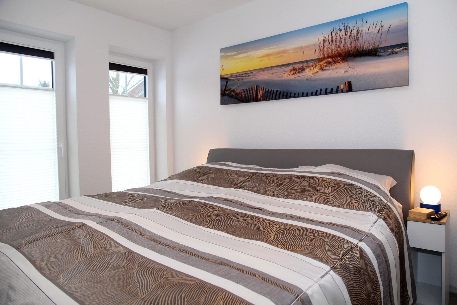 Schlafzimmer mit Bett, Wandbild und Nachttisch.