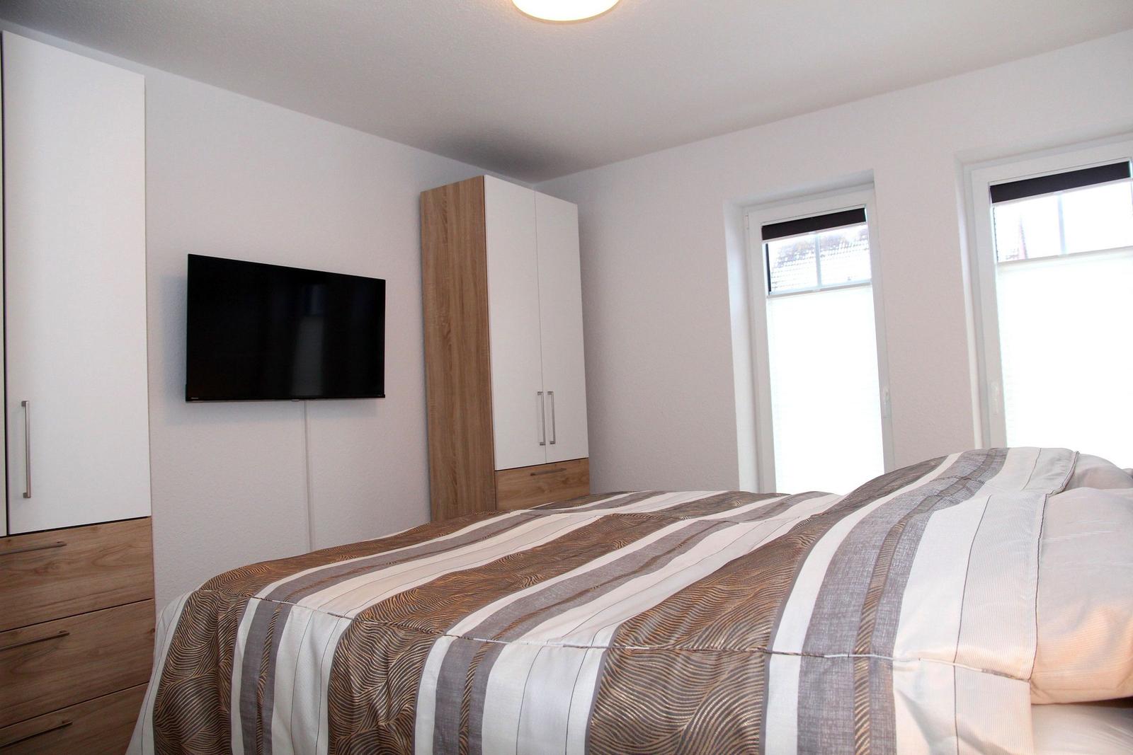 Schlafzimmer mit Bett, TV und Schränken an der Wand.