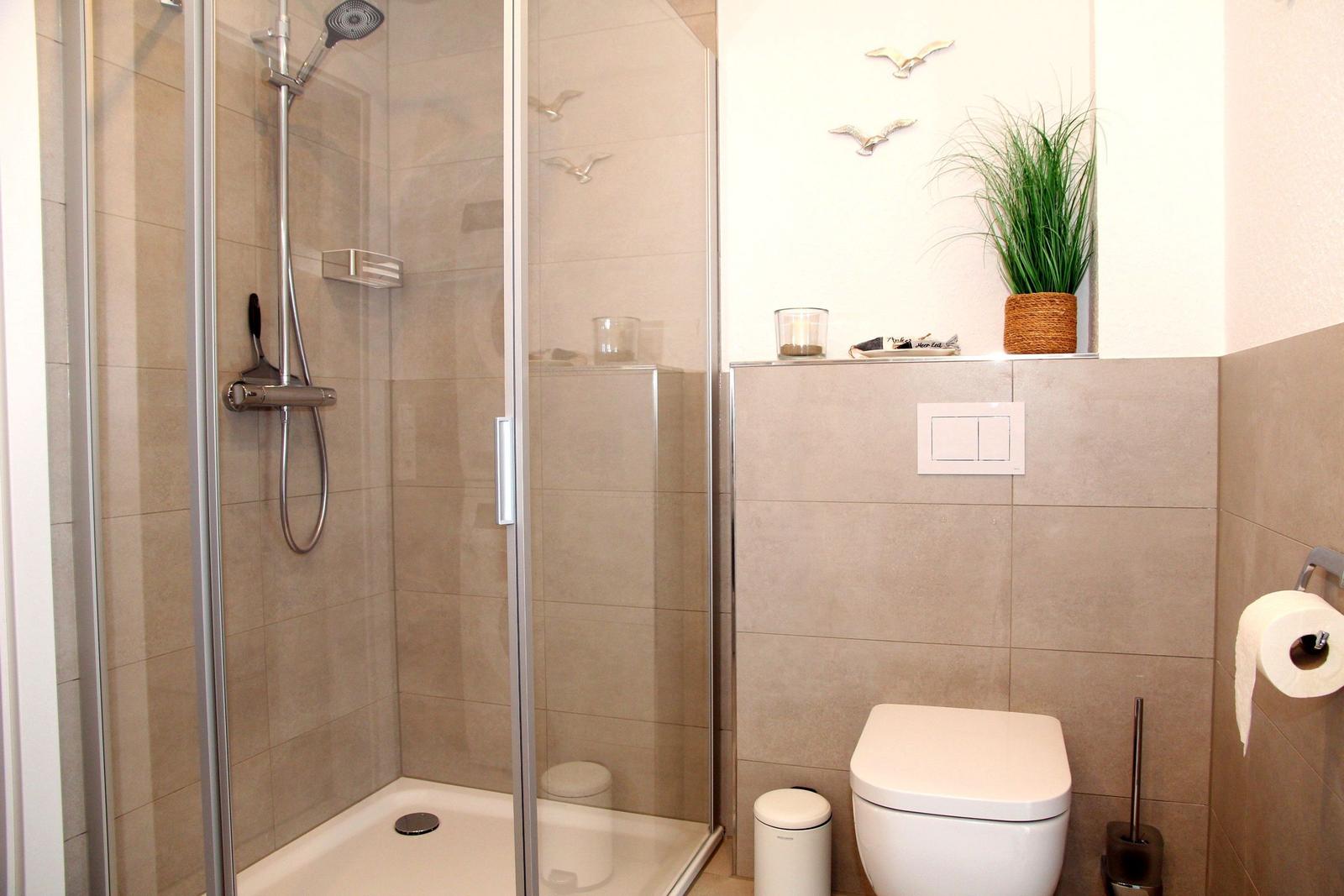 Dusche mit Duschbrause, Toilette und Pflanze an der Wand.