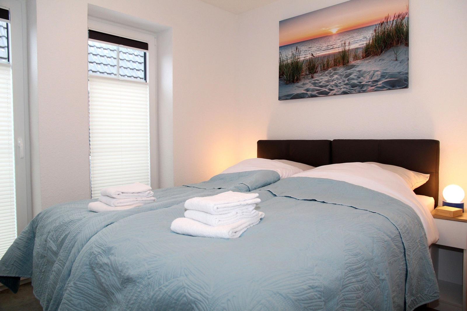 Schlafzimmer mit Bett, Decke und Fenster. Wandbild zeigt Strand bei Sonnenuntergang.