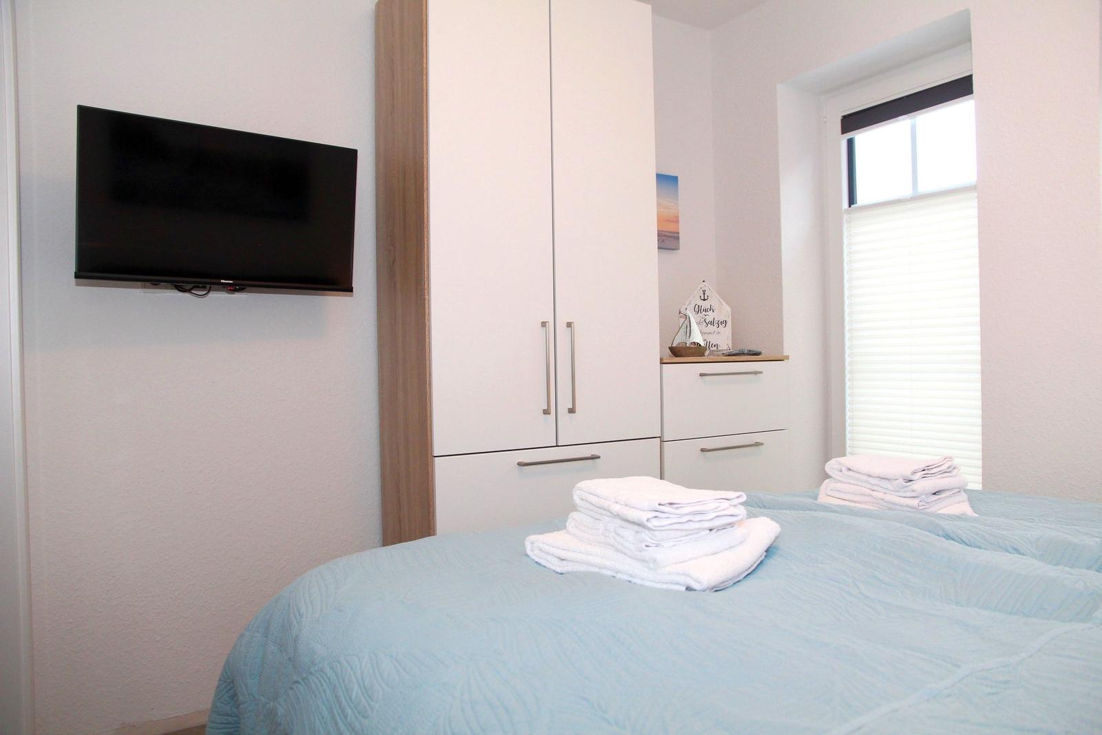 Schlafzimmer mit Bett, TV und Schränken. Fenster mit Jalousie.