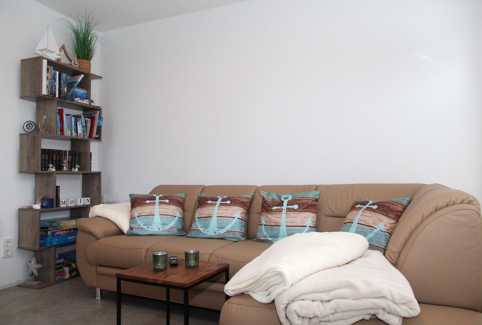Ein Sofa mit Kissen und Decke. Bücherregal mit Dekoration.