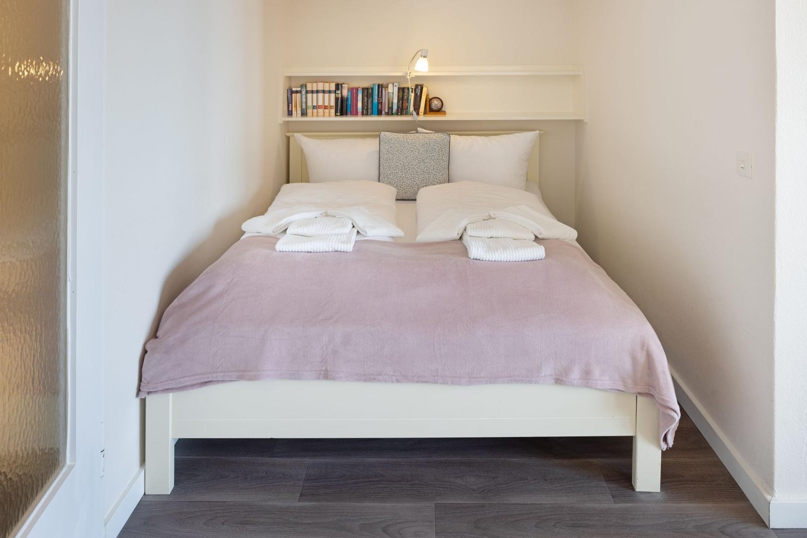 Schlafzimmer mit Bett, Kissen und Bücherregal an der Wand.