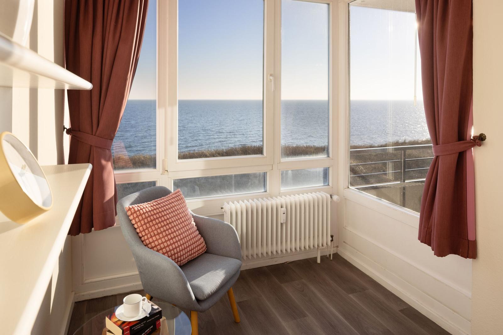 Raum mit Sitzgelegenheit und Meerblick durch große Fenster.